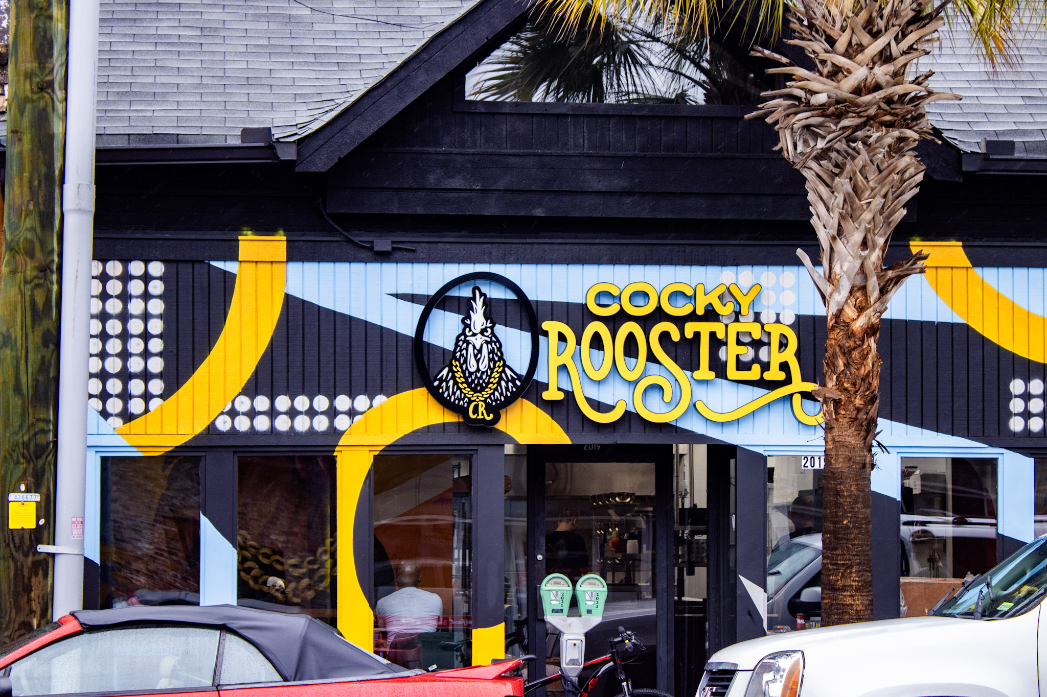 Cocky Rooster storefront on Devine Street in Five Points, Columbia SC, with the yellow and blue mural and palm tree