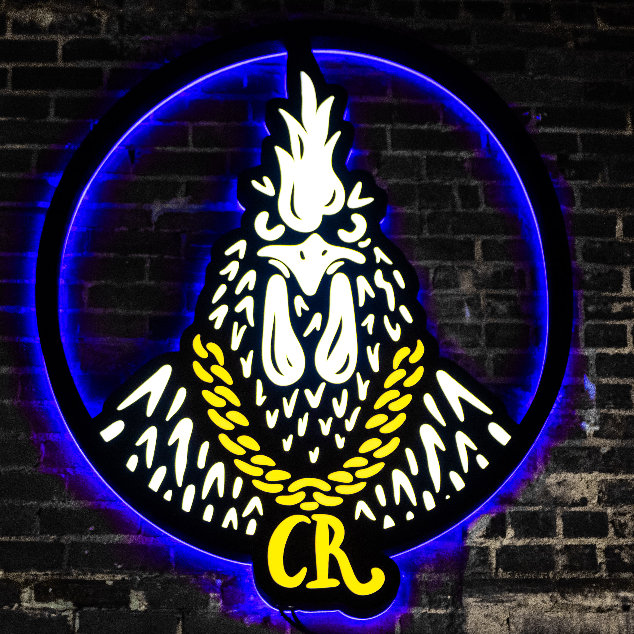 Glowing neon Cocky Rooster logomark on a black brick wall