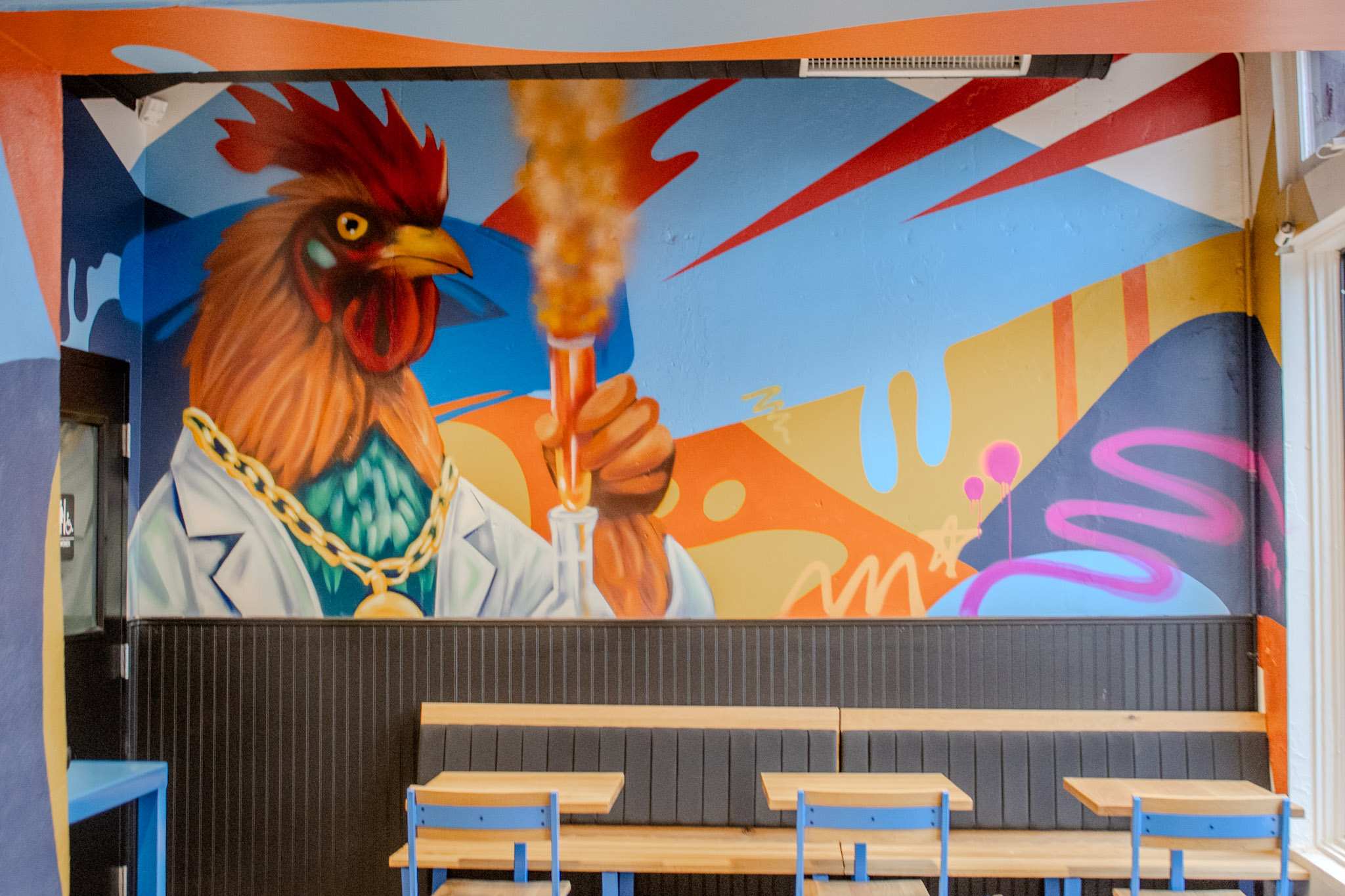 Wide view of the rooster mural and blue-legged wooden tables inside Cocky Rooster Columbia