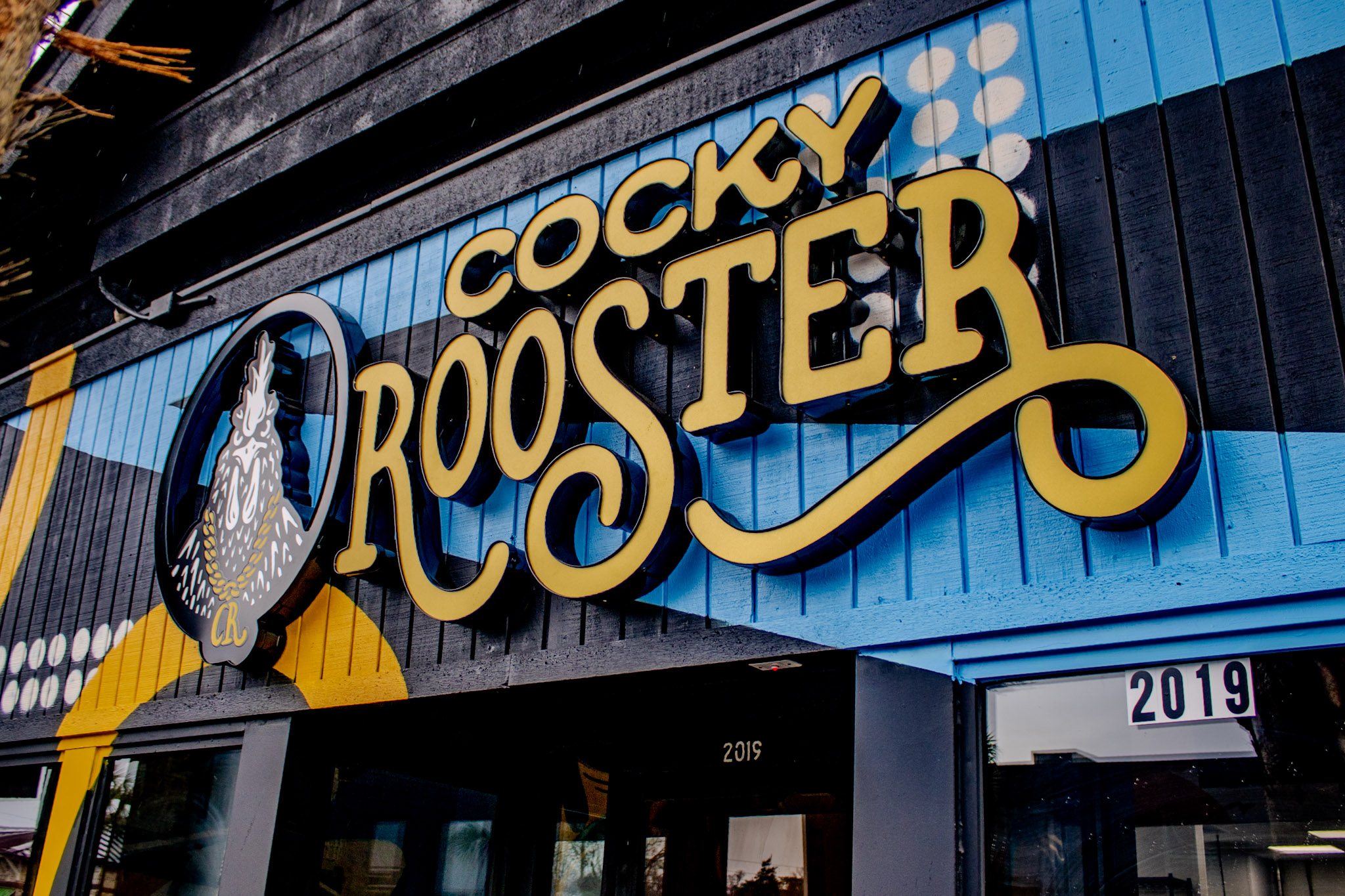 Cocky Rooster sign in yellow script on the black-painted storefront at 2019 Devine St