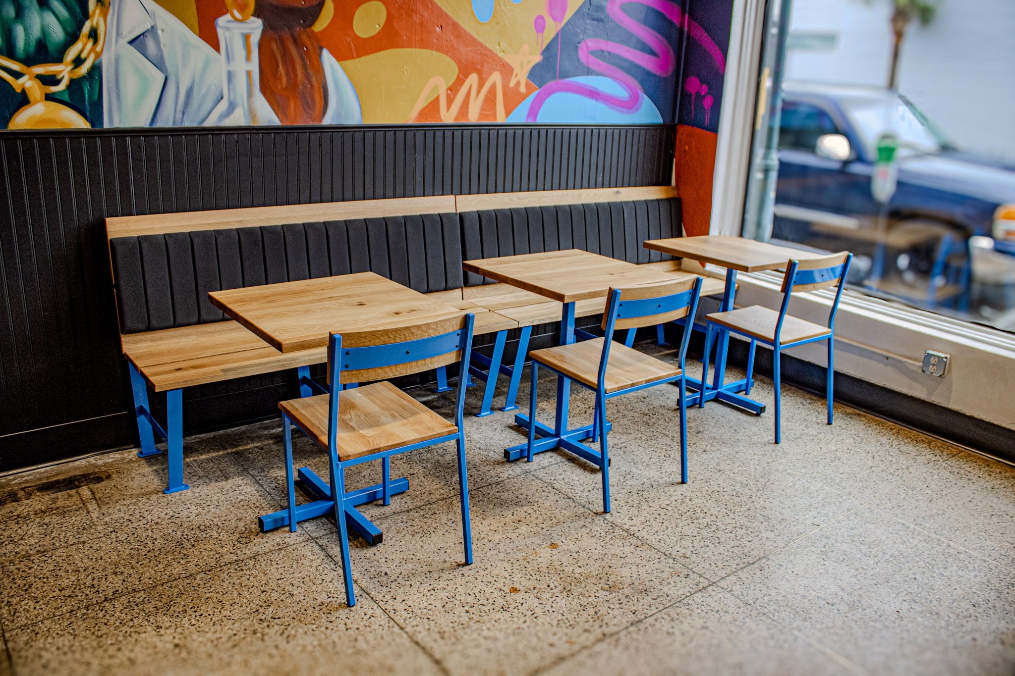 Window seating with wooden tables and blue chairs at Cocky Rooster Devine Street