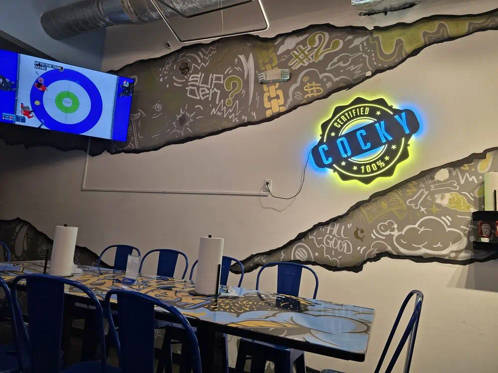 Neon Cocky Rooster badge and blue metal chairs under the doodle mural