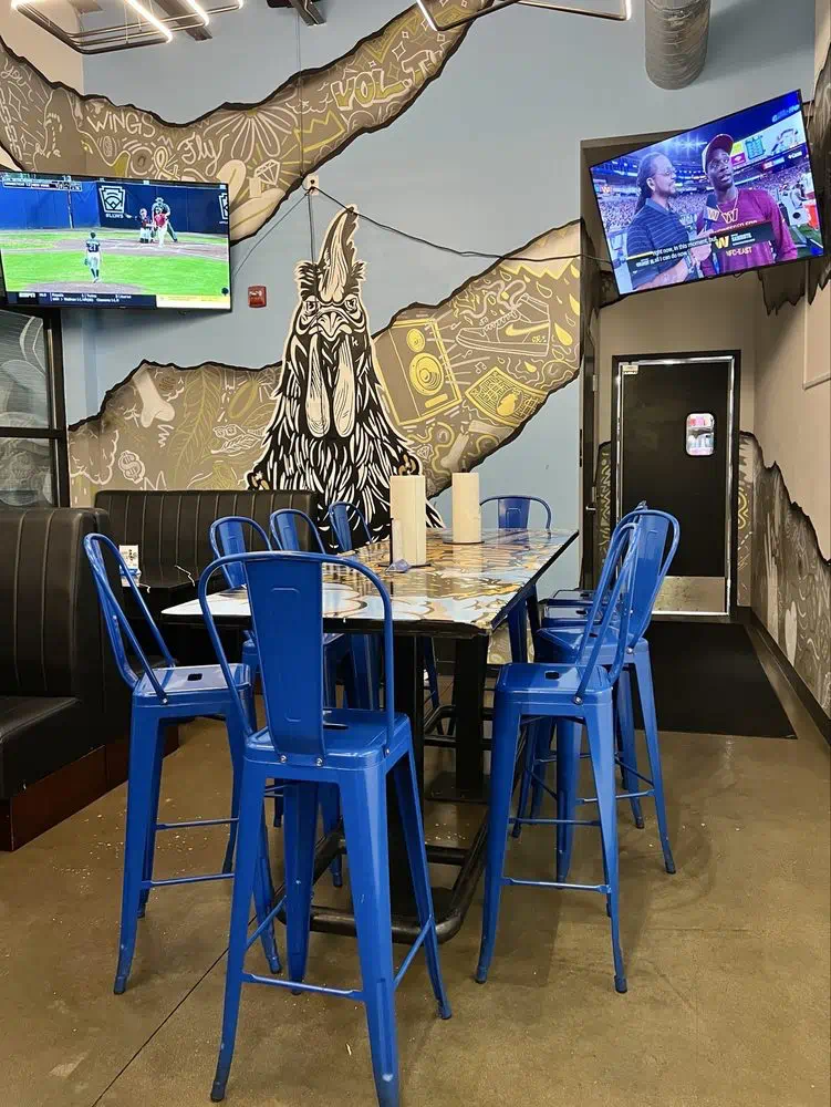 Blue chairs and a booth beneath the black-and-gold rooster mural in the dining room
