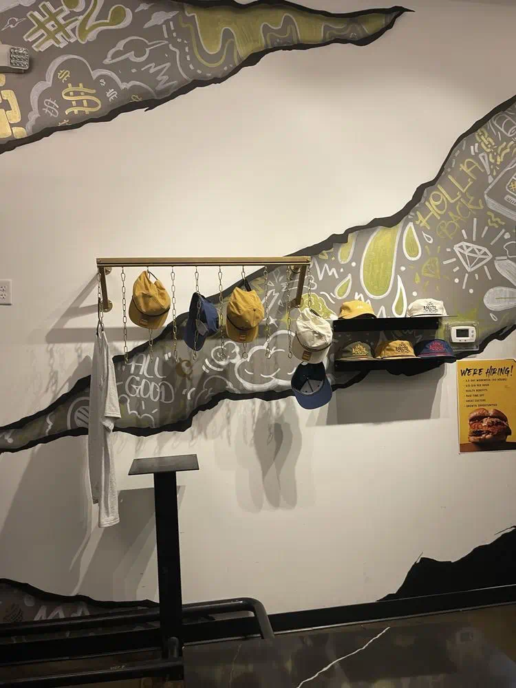 Merch caps hanging on the wall rack beneath the doodle mural