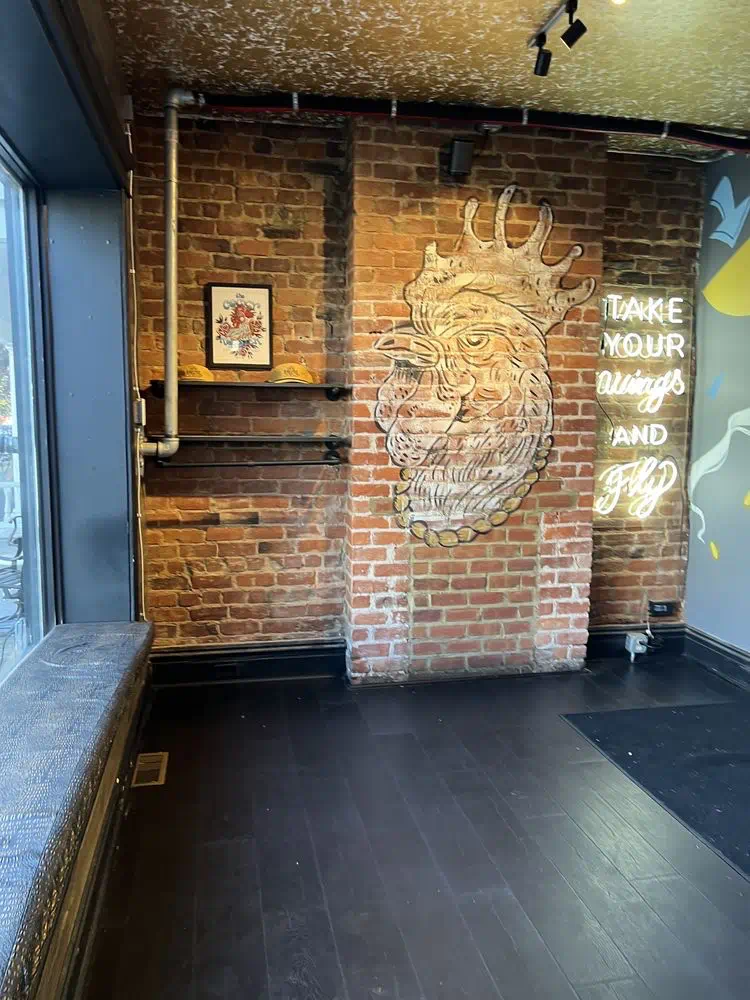 Take Your Wings and Fly neon sign beside the rooster mural on exposed brick