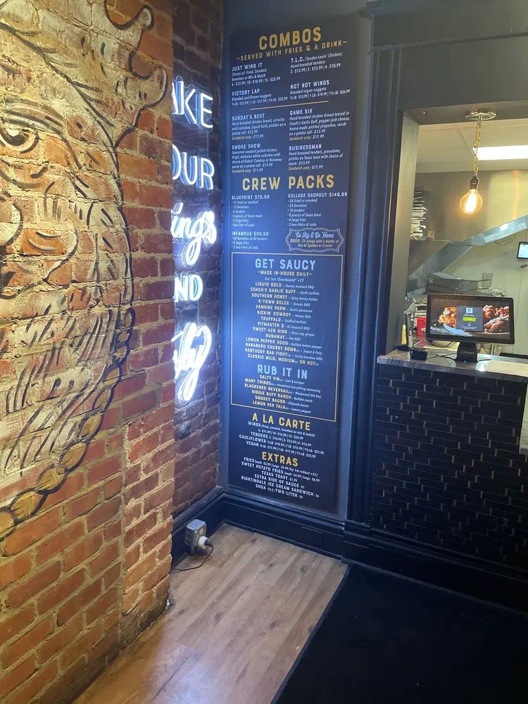 Menu boards for crew packs, sauces and rubs beside the brick rooster mural
